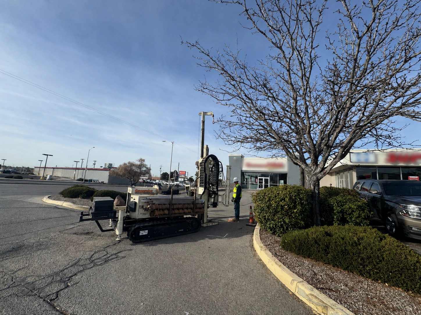 A field technician operates a direct-push drilling rig during Phase II environmental soil and groundwater sampling at a commercial property.